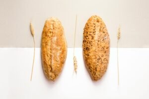 Flat lay image of two artisan bread loaves with wheat decoration on a neutral background.